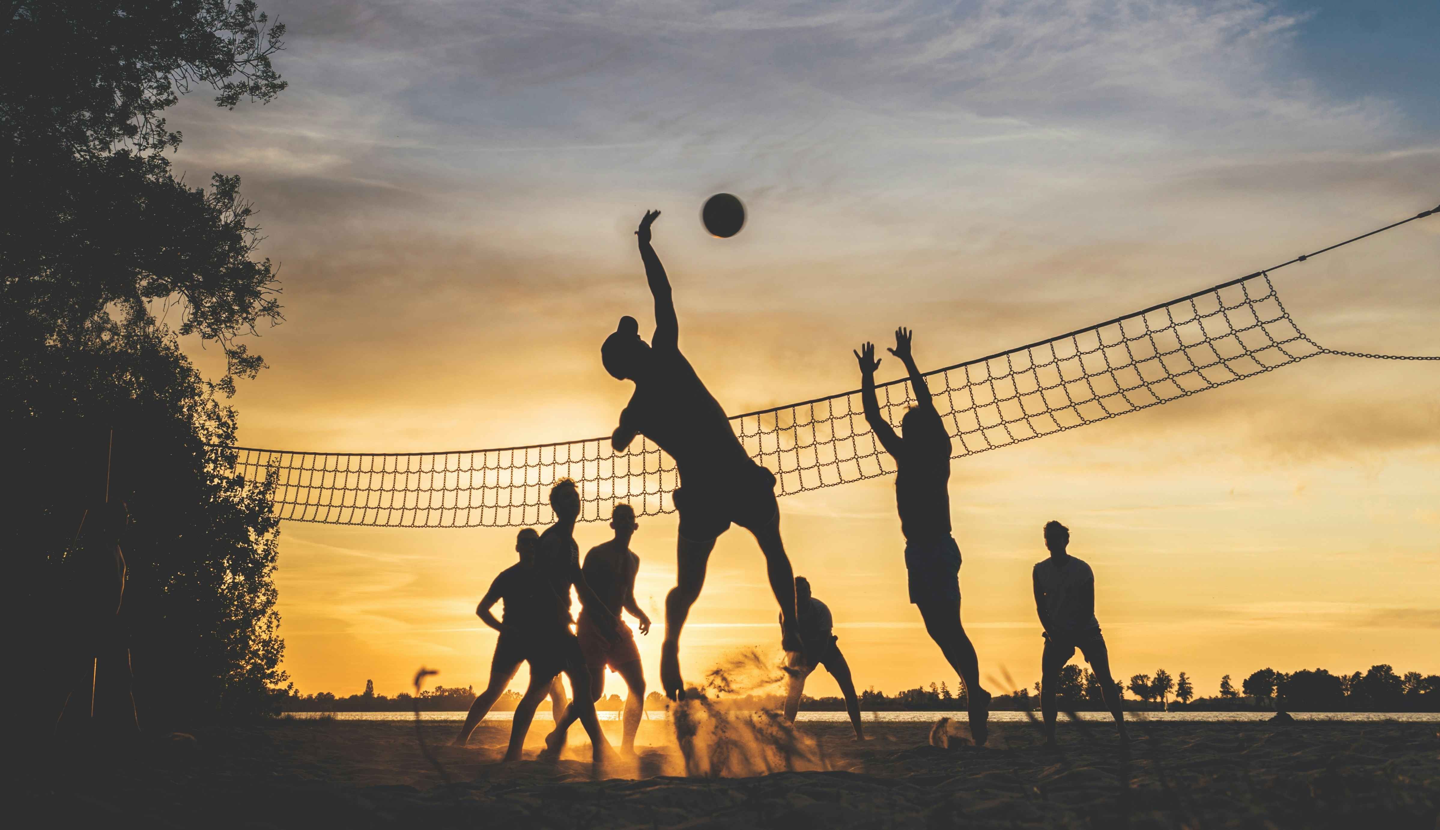 Silhuetas de jogadores de vôlei de praia saltando na rede ao pôr do sol